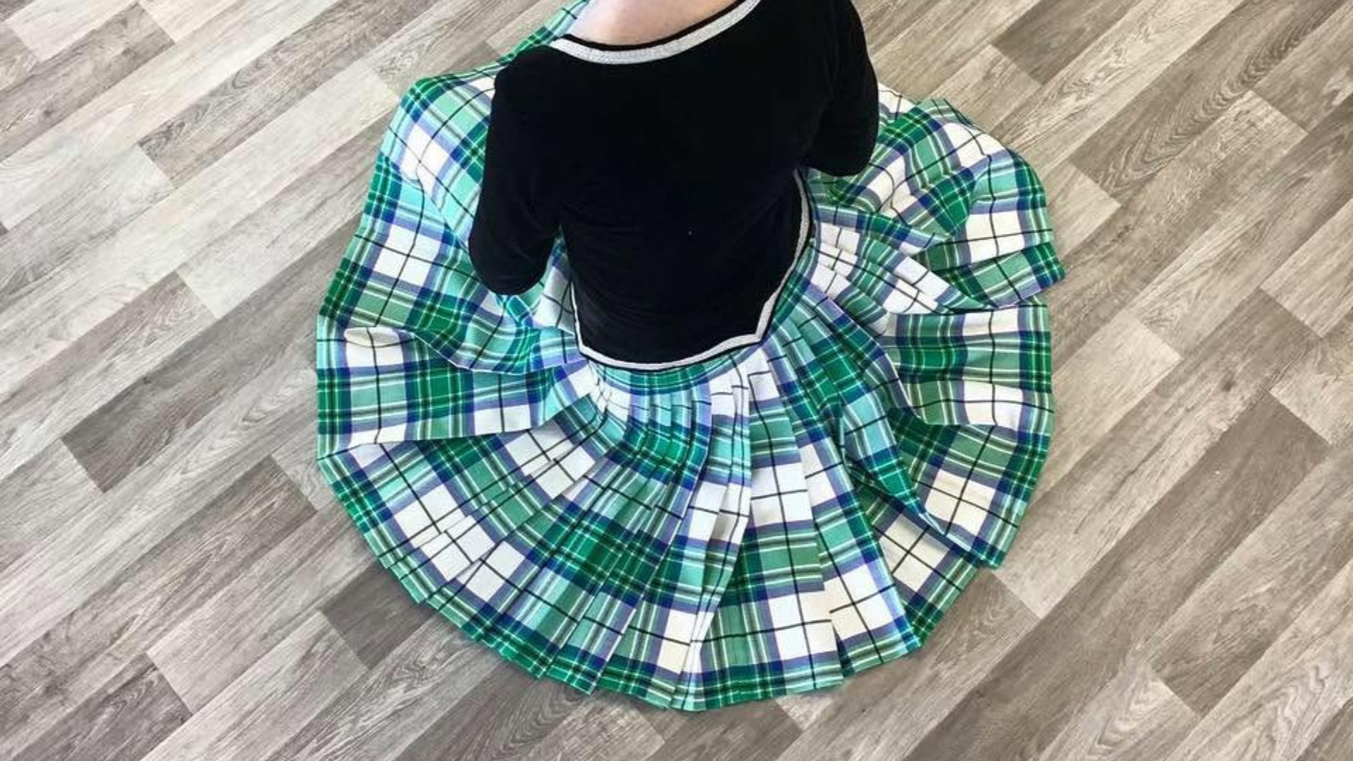 A Highland dancer in a green tartan skirt viewed from above, the pleats fanned out in a full circle